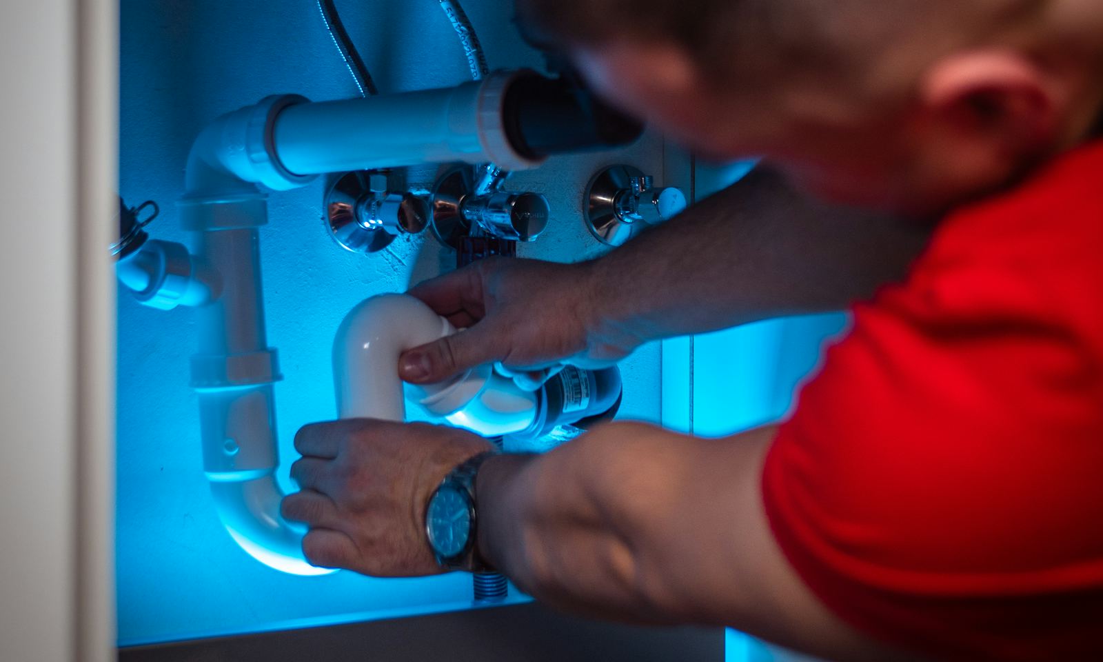 A plumber fitting a new pipe under a kitchen sink