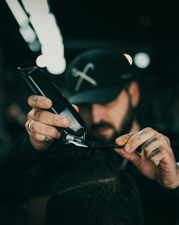 Dan, a bearded barber in a cap, holding scissors